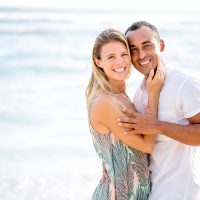 Closeup of adult couple looking at camera and embracing by sea in summer