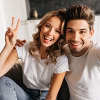 Joyful young man making selfie with his beautiful girlfriend at home. Couple looking at the camera with smile and joy in their eyes.
