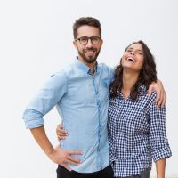 Sweet happy couple hugging each other and laughing. Young woman in casual and man in glasses in glasses posing isolated over white background. Love and friendship concept